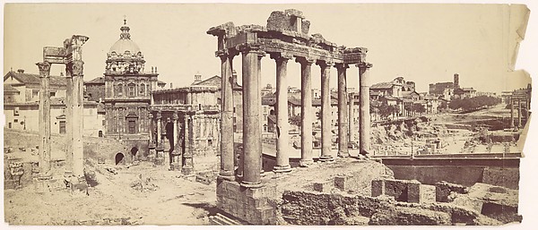 An old photograph of the Roman Forum with tall columns, stone ruins, and open space.