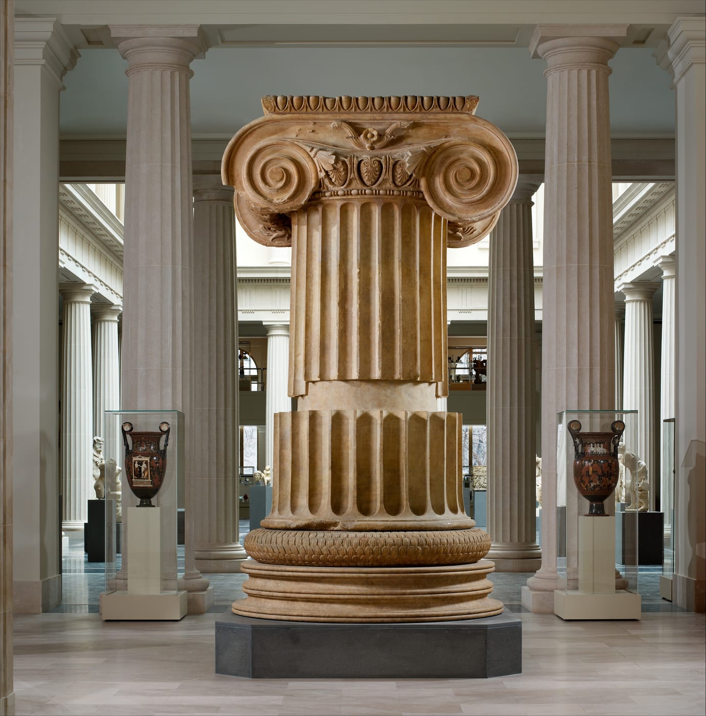 A large marble Greek column with spiral shapes at the top in a museum gallery.