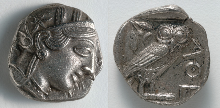 A Greek silver coin showing the head of Athena on one side and an owl with letters on the other side.